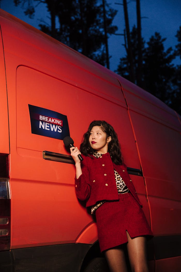service-03 Asian woman reporter in red standing by a breaking news van at twilight.